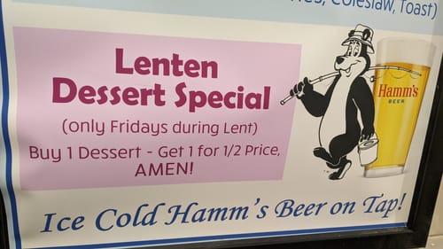 A sign that reads "Lenten Dessert Special (only Fridays during Lent): Buy 1 Dessert - Get 1 for 1/2 Price, AMEN! Ice Cold Hamm's Beer on Tap!" On the right is a picture of the Hamm's bear, a